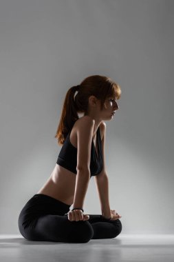 Yoga ve bale çalışmalarından sonra dinlenen ve gerinen kız gri arka planda poz veriyor..