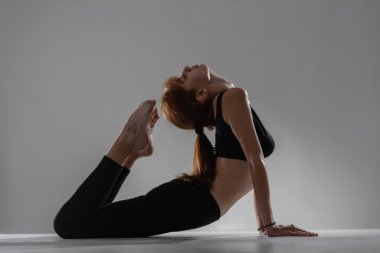 Zinde balerin kız yalan söylüyor ve geriniyor. Gri arka planda yoga pozları veriyor..