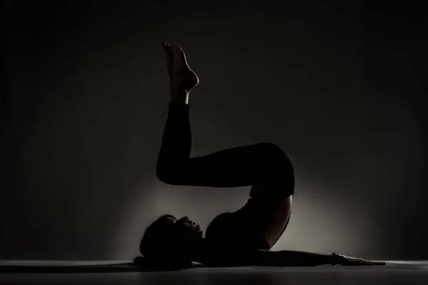 Passform Ballerinaflicka Liggande Och Stretchande Yogaposer Sidobelyst Siluett Mot Mörk — Stockfoto