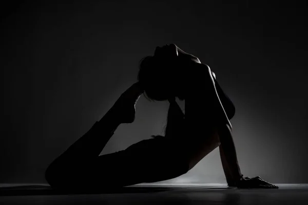 适合芭蕾舞女演员撒谎和伸展练习瑜伽姿势 在黑暗背景下侧面明亮的轮廓 — 图库照片