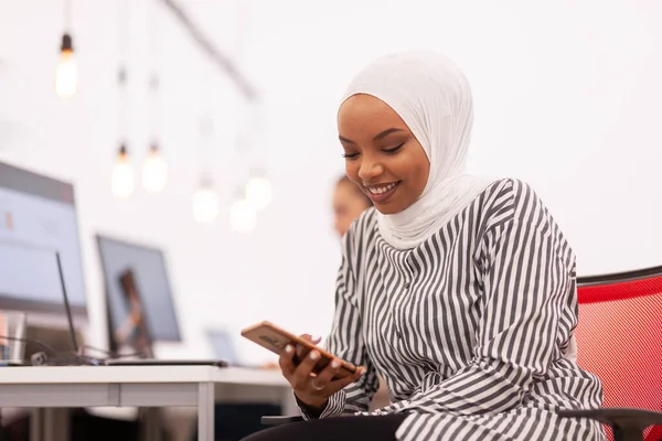 African american muslim girl with hijab working on a phone in modern office. Caucasian girl colleague with headset in the background