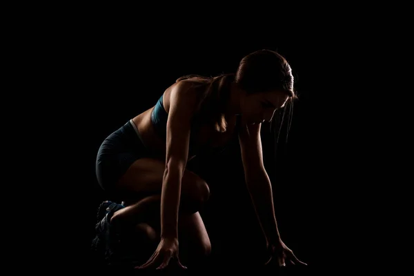 Female runner in low race start position. Girl in sportswear against dark background