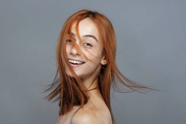 Koyu renkli, turuncu, rüzgarlı, gülümseyen güzel kız. Gri arkaplana karşı gülen yüz ifadesiyle stüdyo portresi.