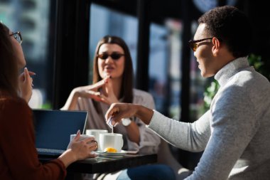 Three friends in a restaurant talking smiling and drinking tea. Business colleagues having a meeting after work or during coffee break at a cafe bar.