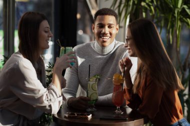 Three multiracial friends in a bar cheering. After work party with cocktails after successful work day.