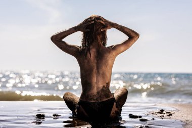 Plajda oturan seksi kız. Vücut kumla kaplı.