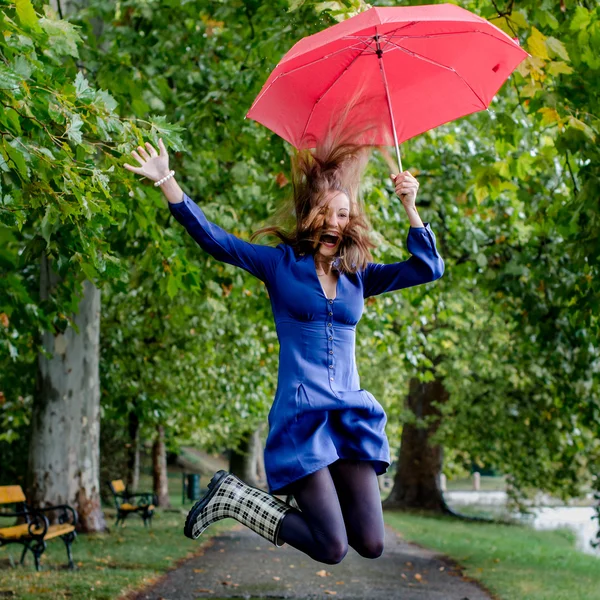 Jonge vrouw springen met rode paraplu — Stockfoto