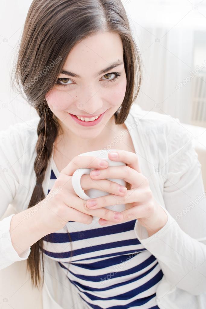 Attractive young woman drinking coffee in couch