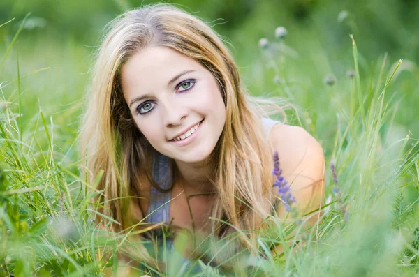 Beautiful young long-haired woman lying in green field — Stock Photo, Image