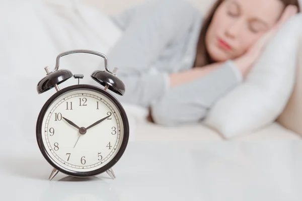 Alarm clock on table and woman sleeping in background — Stock Photo, Image