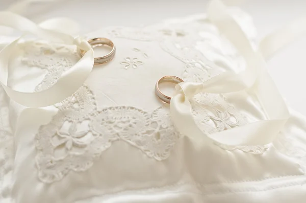 Anelli nuziali dorati su piccolo cuscino bianco — Foto Stock