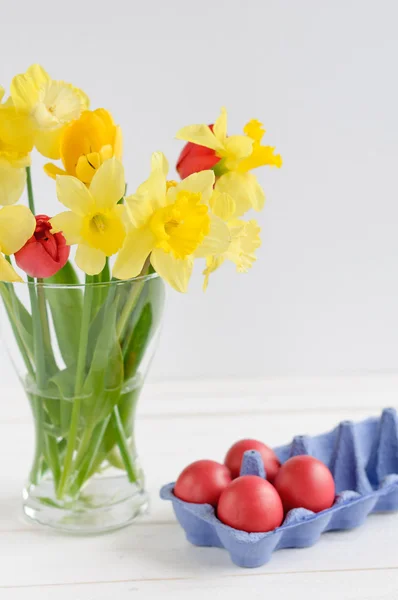 Spring flowers with easter eggs on white wooden background — Stock Photo, Image