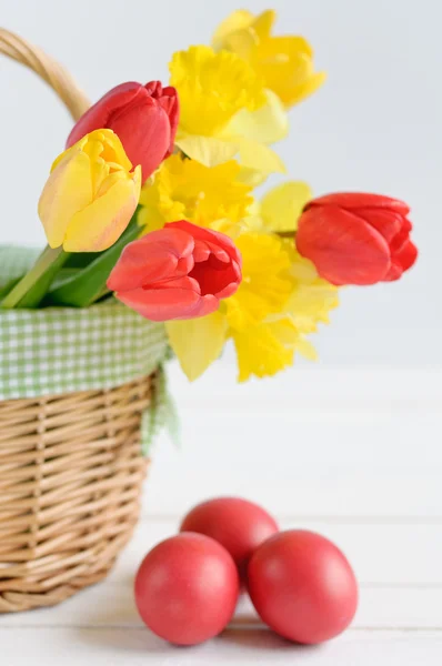 Tulips and daffodils in a basket and colored eggs — Stock Photo, Image