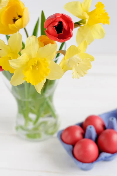 Весняні квіти з великодніми яйцями на білому дерев'яному фоні — стокове фото