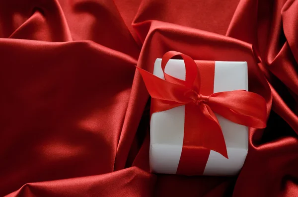 Valentýna dárkové krabice, převázaná červenou saténovou stuhou lukem na červeném pozadí satén — Stock fotografie