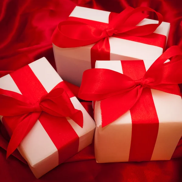 Valentines caixas de presente amarrado com um laço de fita de cetim vermelho no fundo de cetim vermelho — Fotografia de Stock