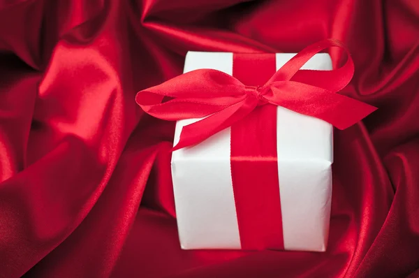 Valentines gift box tied with a red satin ribbon bow on red satin background — Stock Photo, Image