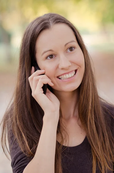 Młoda kobieta uśmiechający się mówi przez telefon komórkowy. — Zdjęcie stockowe