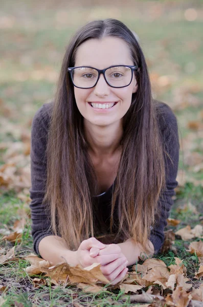 Smiling happy girl lying in autumn leaves. Wearing funny eyeglasses. — Stock Photo, Image