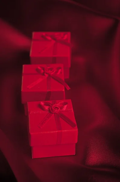 Valentines boîtes-cadeaux attachées avec un ruban de satin rouge noeud sur fond de satin rouge — Photo