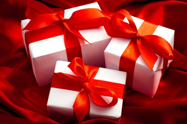 Valentines caixas de presente amarrado com um laço de fita de cetim vermelho no fundo de cetim vermelho — Fotografia de Stock