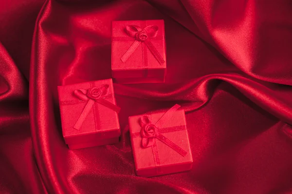 Valentines gift boxes tied with a red satin ribbon bow on red satin background — Stock Photo, Image