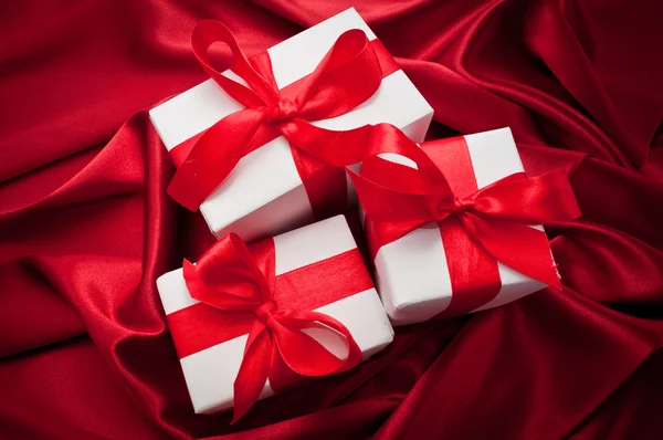 Valentines gift boxes tied with a red satin ribbon bow on red satin background — Stock Photo, Image