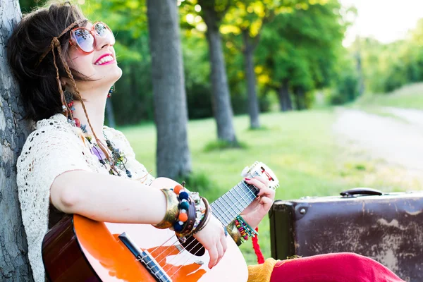 Giovane donna seduta su un campo e suonare la chitarra — Foto Stock