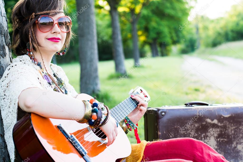 Young woman sitting on a field and playing guitar