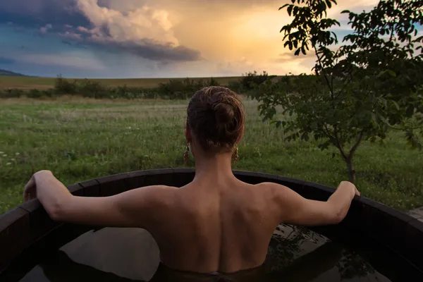 Bathing woman relaxing in outdoor bath or tub and watching sunset — Stock Photo, Image