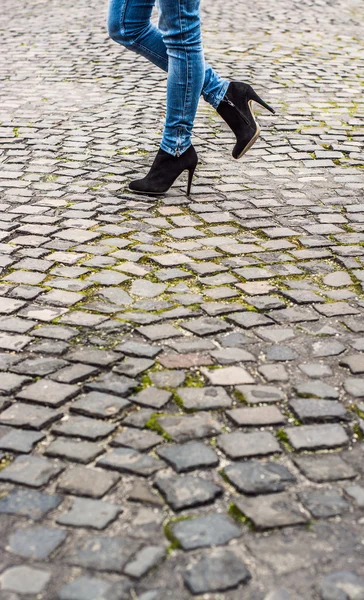 De benen van de vrouw in hoge hak schoenen en blue jeans buiten schot op geplaveide straat — Stockfoto