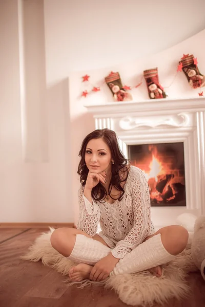 Hermosa joven sentada junto a la chimenea y el árbol de Navidad — Foto de Stock