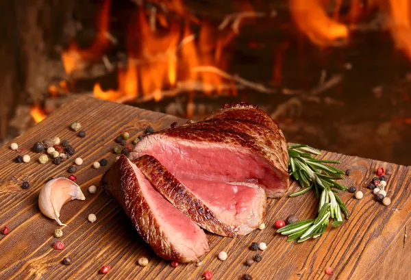 Beef steak on a wooden table on a background of fire — Stock Photo, Image