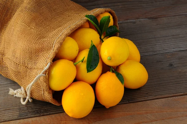 Limones en bolsa de arpillera en madera —  Fotos de Stock