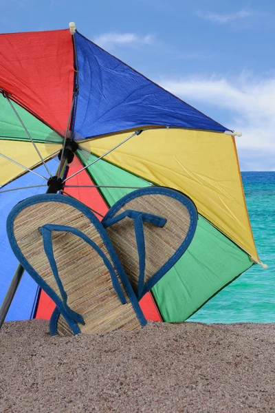 Sandalen und Regenschirm stecken im Sand — Stockfoto