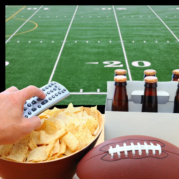 Mano con telecomando TV, birra, patatine e calcio — Foto Stock