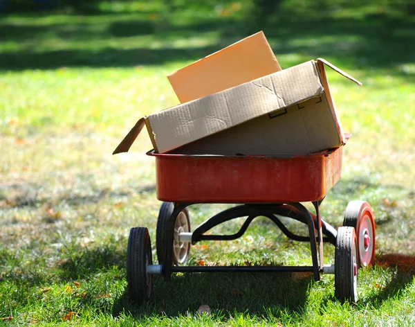 Röd vagn med kartong lådor i park-miljö — Stockfoto