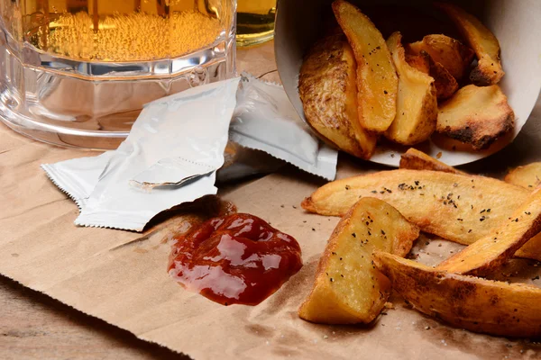 Frites met ketchup op bruine tas en bier — Stockfoto