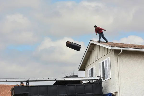 家からトラックへの帯状の帯状の束を投げる労働者は 束が空中にある — ストック写真