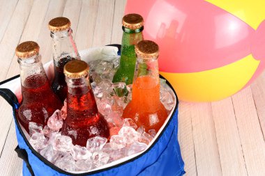 Buzla dolu bir soğutucunun yüksek açılı görüntüsü ve beyaz ahşap zemin üzerinde beachball ile çeşitli soda şişeleri
