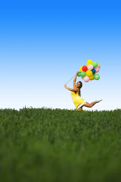 Jeune femme avec des ballons colorés sur une prairie verte — Photo