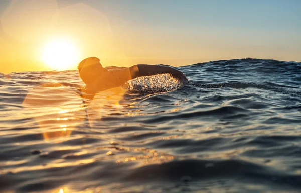 Junger Mann schwimmt im Meer über gelbem Sonnenaufgang — Stockfoto