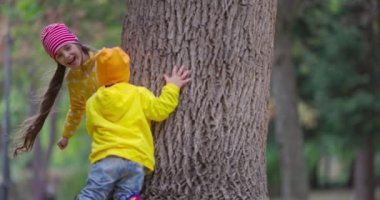 Mutlu çocuklar, erkek ve kız dışarıda oynuyorlar, bir yuhalamaya bakıyorlar ve büyük sonbahar ağacının etrafında saklanıyorlar.