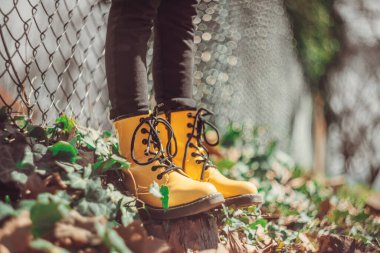 Yeşil çimenlikte zıplayan bir kızın sarı çizmeleri, klasik lensli defocus bokeh.