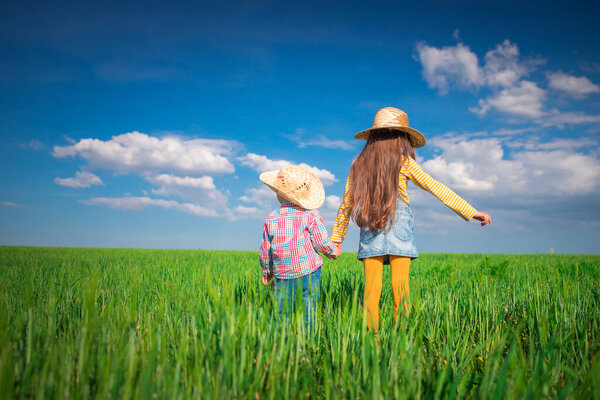 Green wheat field landscape and happy farmer girl and boy playing with straw hat