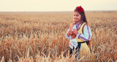 Beautiful girl woman in traditional Bulgarian folklore dress holding homemade bread in wheat field, agriculture and homegrown food concept