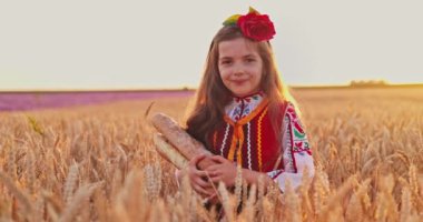 Beautiful girl woman in traditional Bulgarian folklore dress holding homemade bread in wheat field, agriculture and homegrown food concept