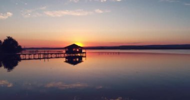 Moving slowly and smoothly over a lake fishing dock and old bungalow in the sea water during beautiful sunset 
