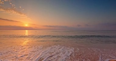 Ocean beach sunrise with color sky clouds and sun rays over sea waves, 4K video landscape. Footprints in the sand.