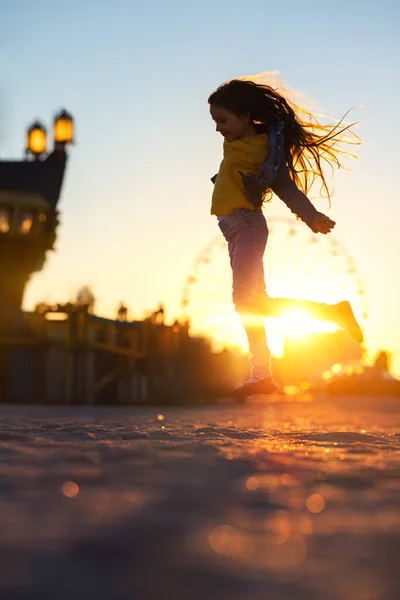 ビーチの砂の上をジャンプし 楽しい街で夕日を楽しむ幸せな女の子 — ストック写真